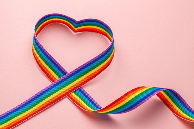 Photo lgbt rainbow ribbon in the shape of heart. pride tape symbol. pink background.