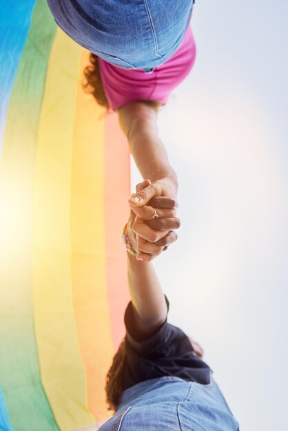 LGBTQ community rainbow flag and couple holding hands for human rights protest solidarity and gay lesbian support Queer sky and black people together in love partnership and equality below view