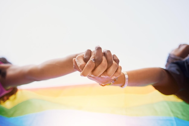 LGBTQ flag rainbow and couple holding hands for gay pride lesbian support or human rights protest LGBT community sky and African black people together in love partnership and equality below view