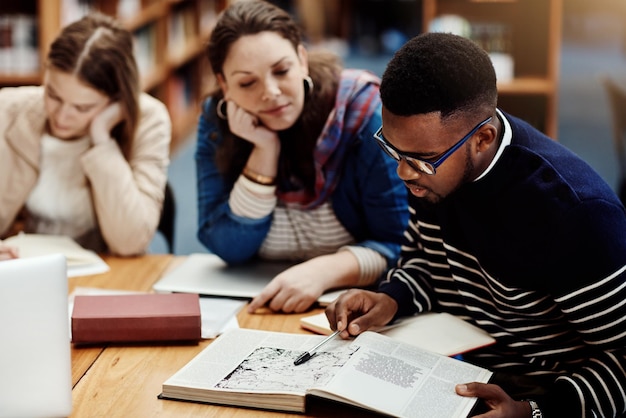 Library people and studying with book research and reading for exam woman and man in campus of college Students friends and teamwork for test information and table with project and together