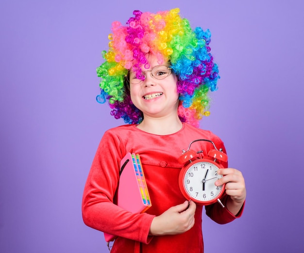 Life is fun Happy childhood Happy little girl International childrens day Child care Happy moments Kid hold alarm clock Girl cute playful kid wear curly rainbow wig Take care of your time