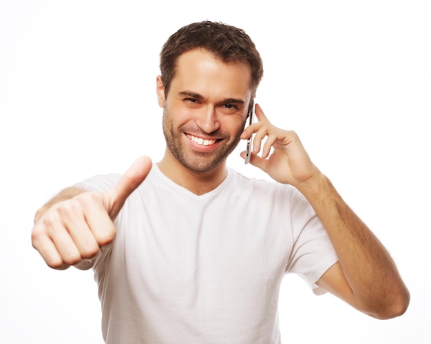 Life style, business  and people concept: casual young man showing thumbs up sign, while speaking on the phone and smiling to the camera. Isolated on white background