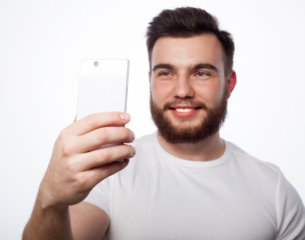 Life style, happiness and people concept: young bearded man with mobile phone in hand against grey background.