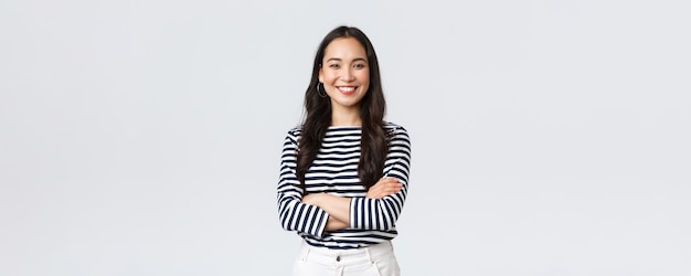 Lifestyle beauty and fashion people emotions concept Young asian female office manager CEO with pleased expression standing over white background smiling with arms crossed over chest