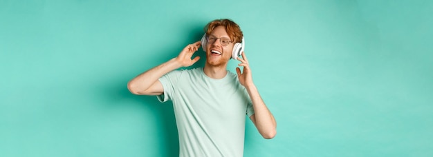 Lifestyle concept happy young man with ginger hair dancing and having fun listening music on wireles