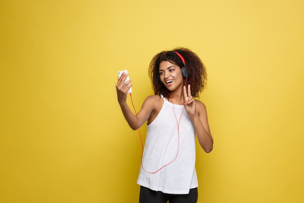 Lifestyle Concept - Portrait of beautiful African American woman joyful listening to music on mobile phone. Yellow pastel studio background. Copy Space.