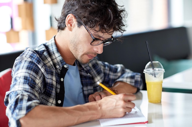 lifestyle, creativity, freelance, inspiration and people concept - creative man with notebook or diary writing and drinking juice at cafe