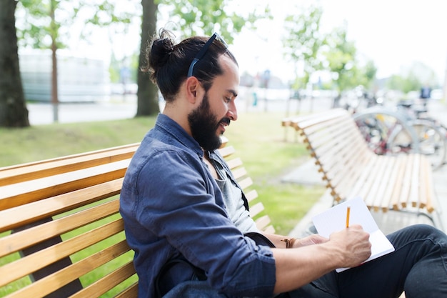 lifestyle, creativity, freelance, inspiration and people concept - creative man with notebook or diary writing sitting on city street bench