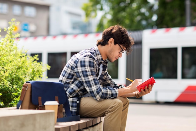 lifestyle, creativity, freelance, inspiration and people concept - creative man with notebook or diary writing sitting on city street bench