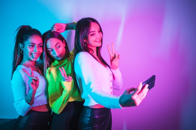 Lifestyle of friends partying in a disco with blue and pink neon lights taking a selfie with the phone for social networks