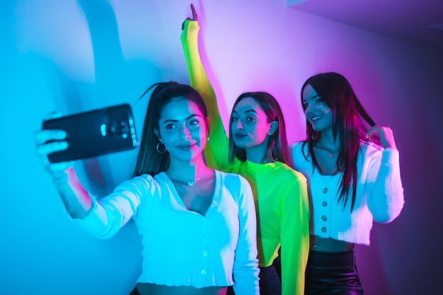 Lifestyle of friends partying in a nightclub with blue and pink neon lights taking a selfie with the phone