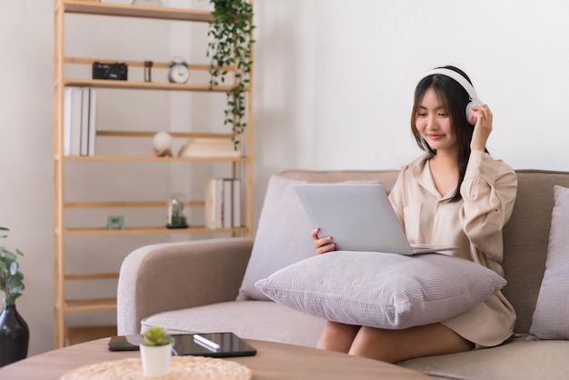 Lifestyle at home concept Young Asian woman is wearing headphone and listening music on laptop