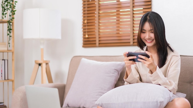 Lifestyle at home concept Young Asian woman use smartphone to playing games while sitting on sofa