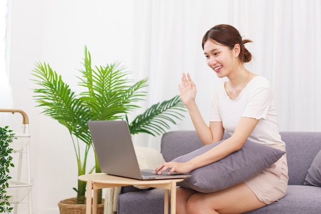 Lifestyle in living room concept Asian woman makes greeting gesture with colleague on video call