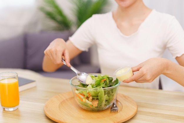 Lifestyle in living room concept Asian woman using spoon to ladle salad dressing into salad bowl