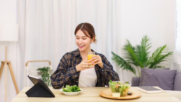 Lifestyle in living room concept Asian woman watching movie on tablet and drinking orange juice