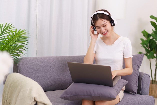 Lifestyle in living room concept Young Asian woman in headphone to listening music on laptop