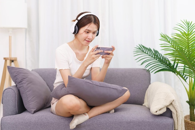 Lifestyle in living room concept Young Asian woman in headphone to playing games on smartphone