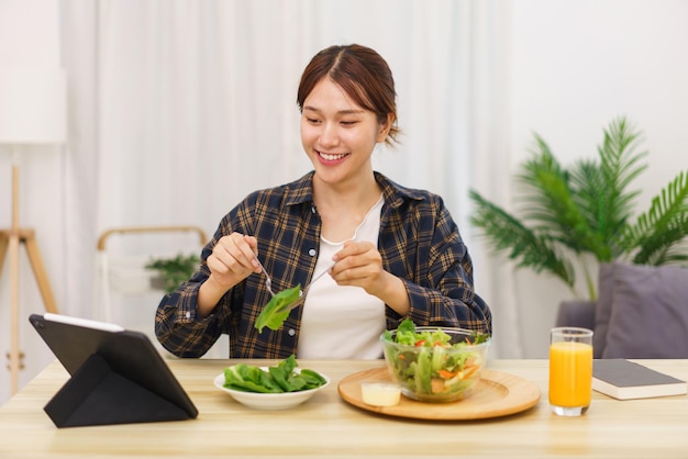 Lifestyle in living room concept Young Asian woman looking at tablet and eating vegetable salad