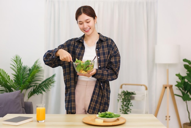 Lifestyle in living room concept Young Asian woman standing to mixing vegetable salad in bowl