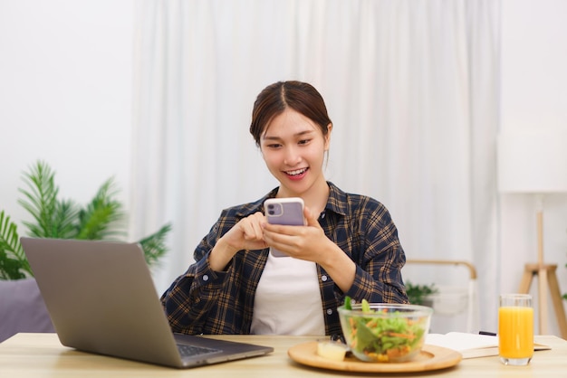 Lifestyle in living room concept Young Asian woman using smartphone and eating vegetable salad