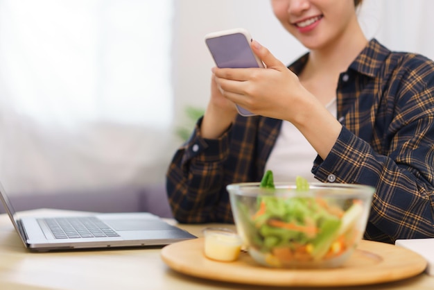 Lifestyle in living room concept Young Asian woman using smartphone and eating vegetable salad