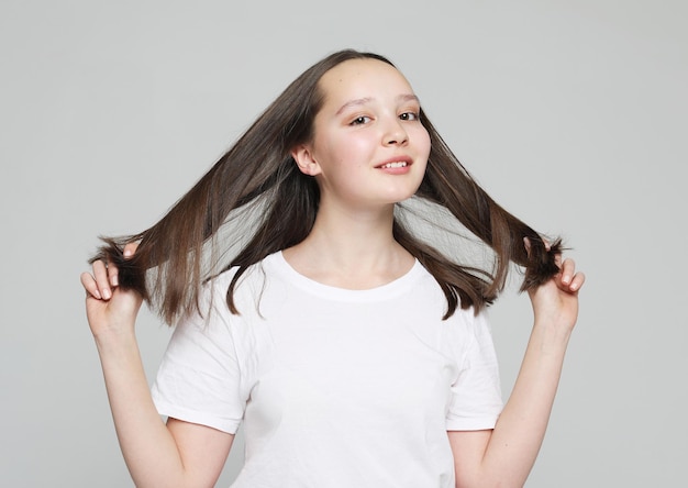 Lifestyle and people concept Beautiful happy female touches her hair Wearing White shirt Over grey background