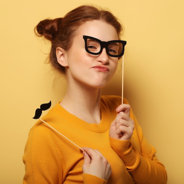 Lifestyle and people concept Happy girl wearing fake mustaches and glasses over yellow background