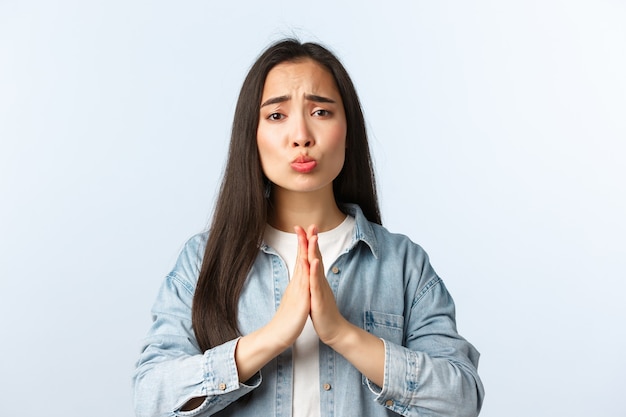 Lifestyle, people emotions and beauty concept. Silly and cute pleading asian girl begging for favour or apology, grimacing looking sad eyes, hold hands in pray as need help, white background