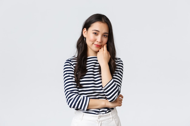 Lifestyle, people emotions and casual concept. Gorgeous smiling young asian woman lean on palm gently looking camera, listening to conversation, standing white background