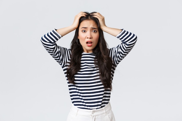 Lifestyle, people emotions and casual concept. Troubled young woman stare alarmed, feel bad as something awful happened, grab head and stare camera anxious, white background