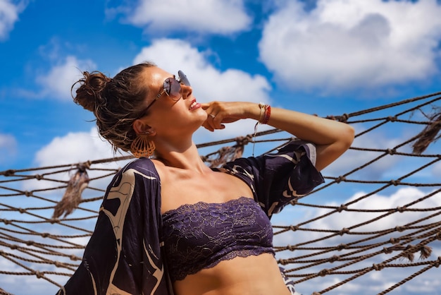 Lifestyle portrait happy female in sunglasses resting in hammock looking up