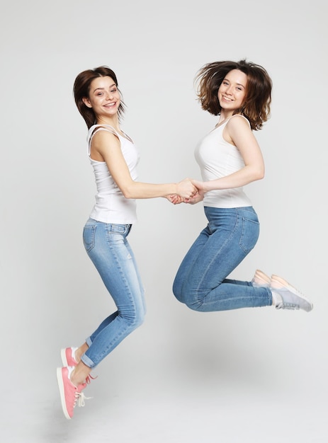 Lifestyle portrait of two young women best friends jump over white background