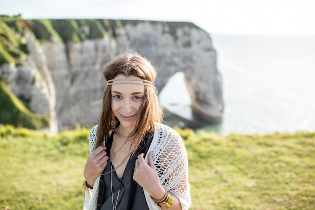 Lifestyle portrait of a young woman dressed in hippie style enjoying nature on the rocky coastline with great view on the ocean in France