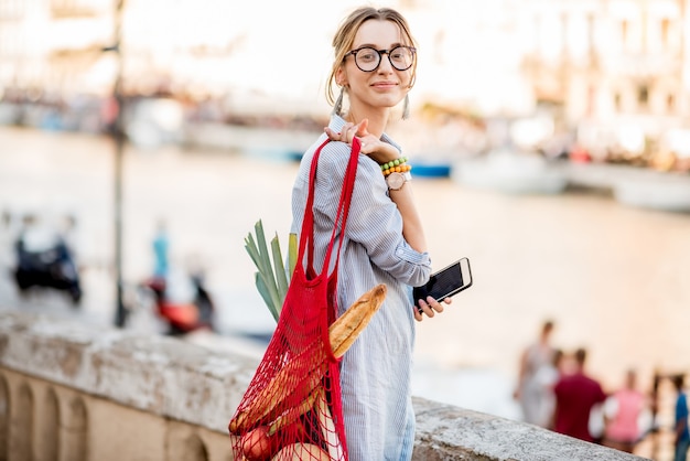 Lifestyle portrait of a young woman with mesh bag full of fresh food oudoors in the old city