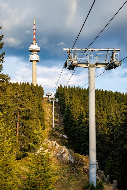 Lift with cable passes between spruce forest on peak against backdrop of mountain ranges of Rhodope Mountains