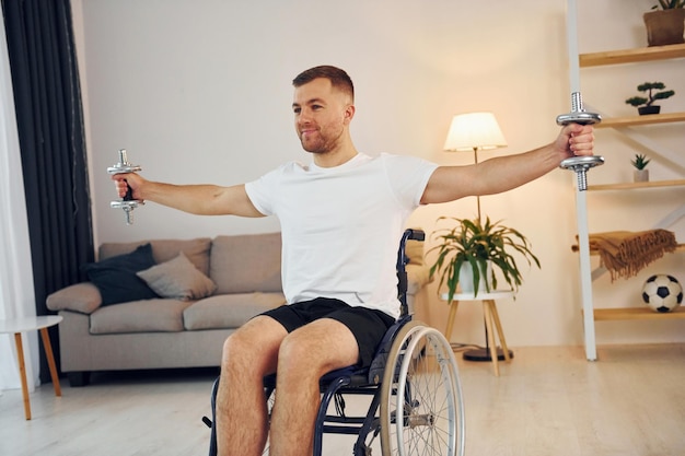 Lifting dumbbells Disabled man in wheelchair is at home