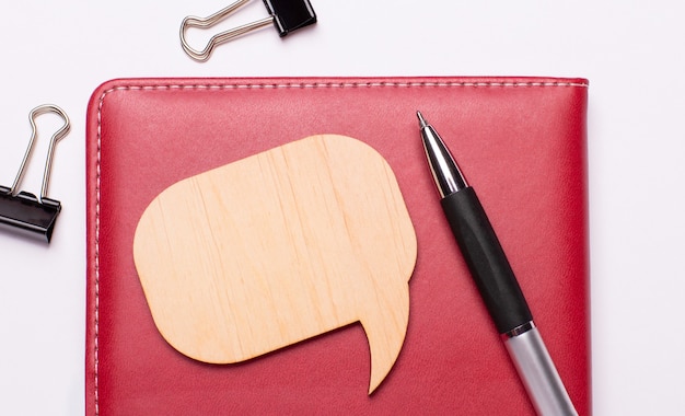 On a light background - black paper clips, a pen, a burgundy notebook and a wooden plaque with a place to insert text. Template.