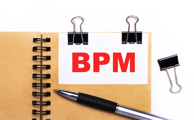 On a light background a brown notebook with a pen black clips and a white card with the text BPM Business Process Management