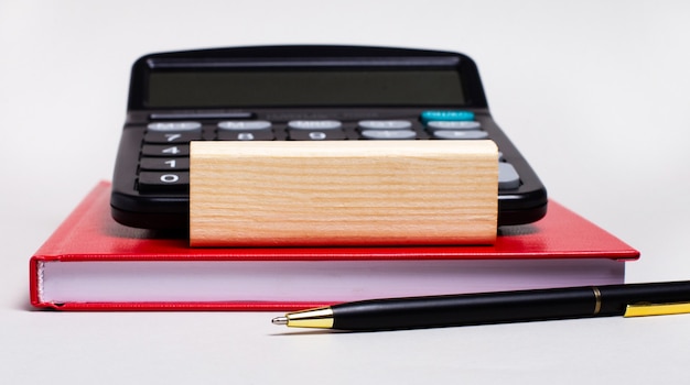 On a light background, a burgundy notebook, a calculator, a pen and a wooden block with a place to insert text.