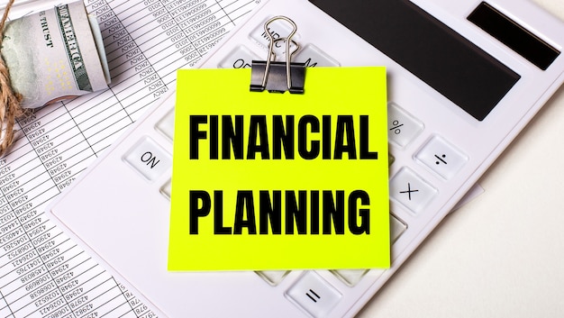 On a light background - cash, a white calculator and a yellow sticker under a black paper clip with the text FINANCIAL PLANNING. Business concept