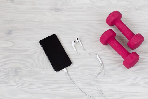 Photo on a light background mobile phone, headphones and dumbbells