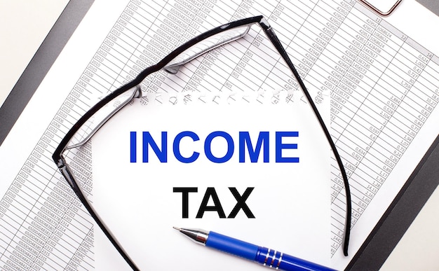 On a light background a report blackframed glasses a pen and a sheet of paper with the text INCOME TAX Business concept