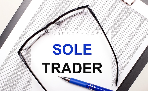 On a light background a report blackframed glasses a pen and a sheet of paper with the text SOLE TRADER Business concept