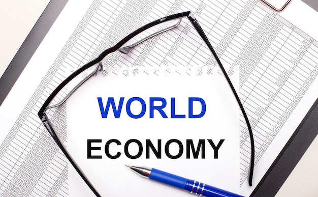 On a light background a report blackframed glasses a pen and a sheet of paper with the text WORLD ECONOMY Business concept