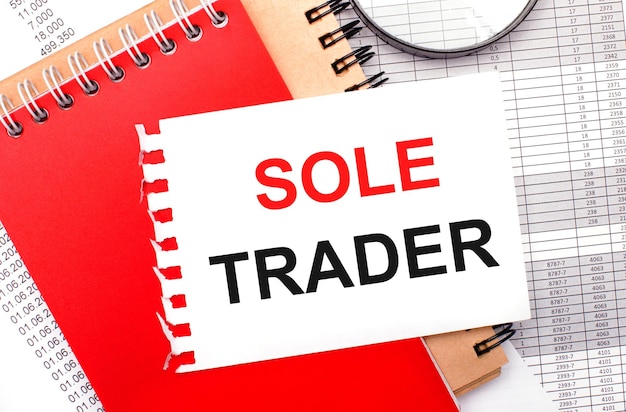 On a light background reports a magnifying glass brown and red notepads and a white notepad with the text SOLE TRADER Business concept