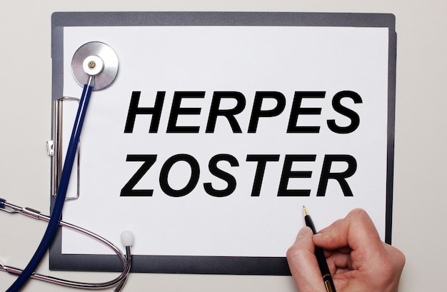 On a light background, a stethoscope and a sheet of paper, on which a man writes HERPES ZOSTER. Medical concept