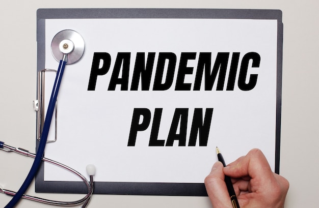 Photo on a light background, a stethoscope and a sheet of paper, on which a man writes pandemic plan. medical concept