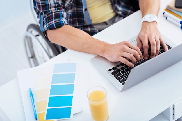 Light colors. Competent worker using computer while typing article, sitting in his wheelchair