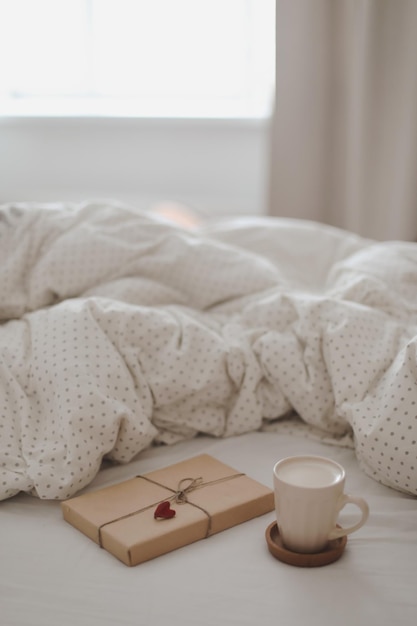 Light cozy bedroom Cup of aromatic coffee book and warm plaid on bed with soft blanket indoors top view